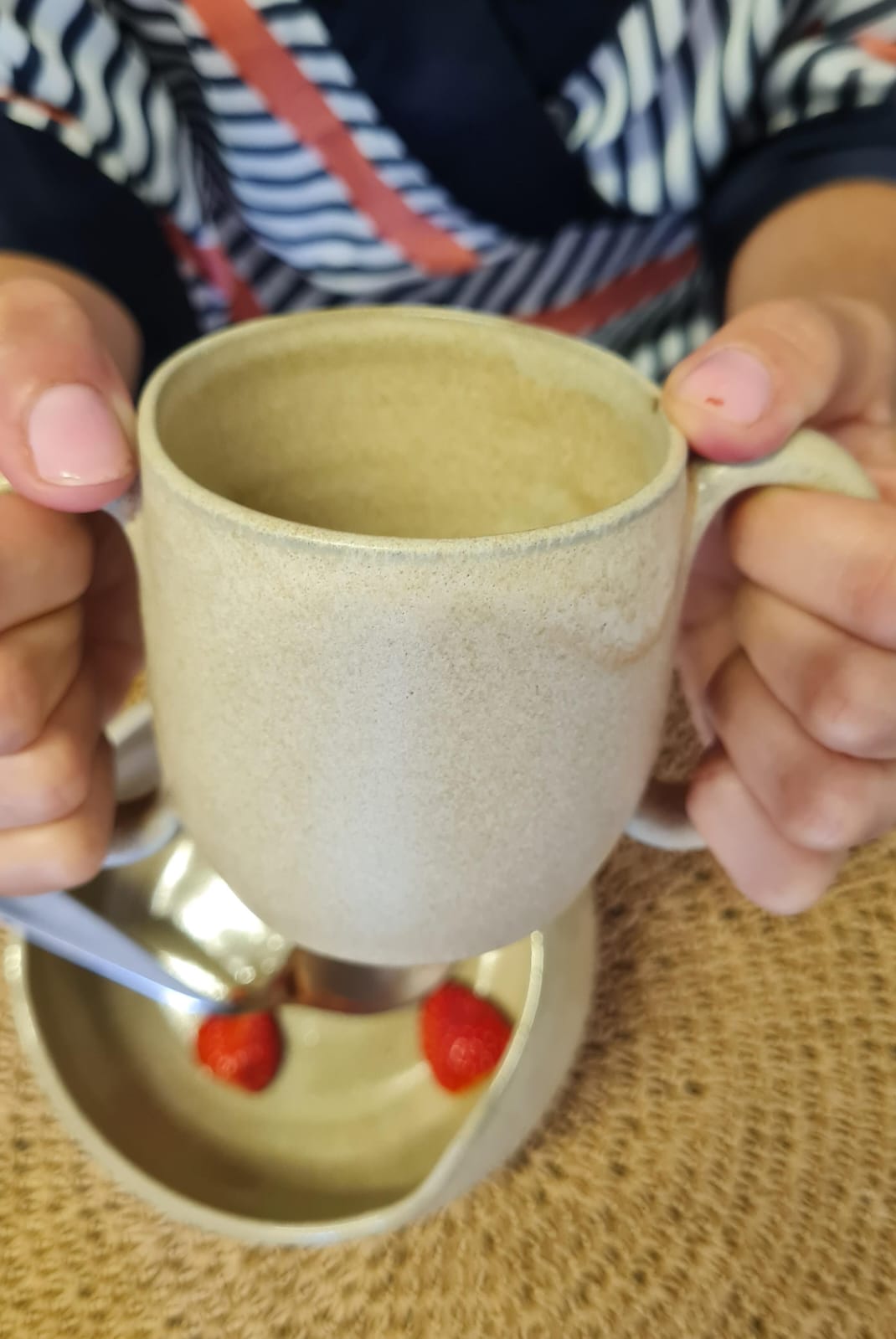 Mãos segurando a caneca de dupla alça sobre um bowl com morangos